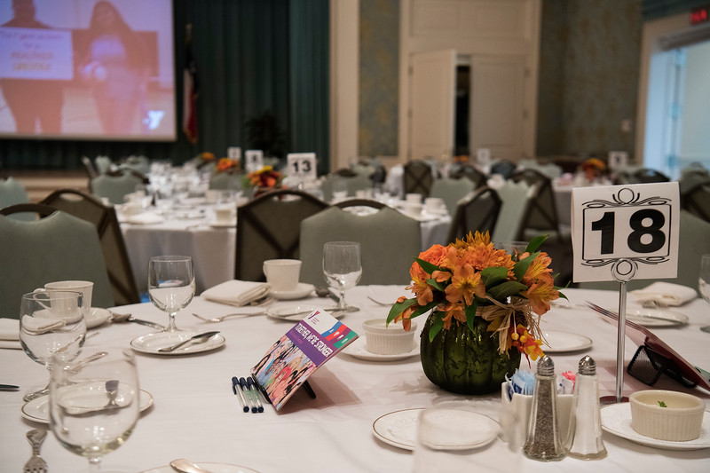 A formal banquet table displaying a number '18' card next to a bouquet of orange flowers at the Annual Celebrating of Women Luncheon at the Y