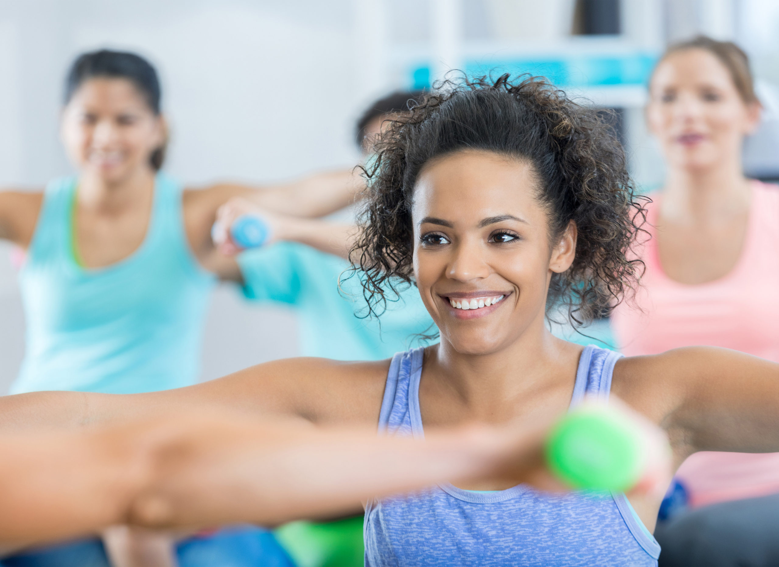 Smiling young woman works arms in weight training exercise class