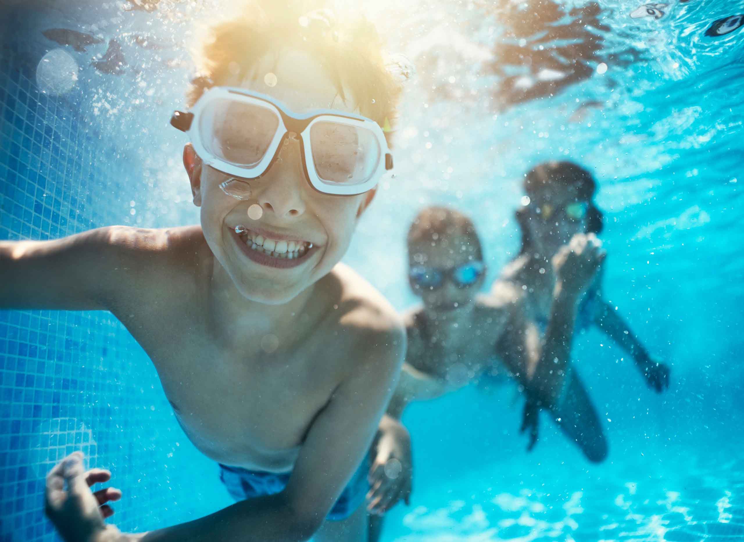 A photo of chidren swimming underwater in a pool with blue tiles.
