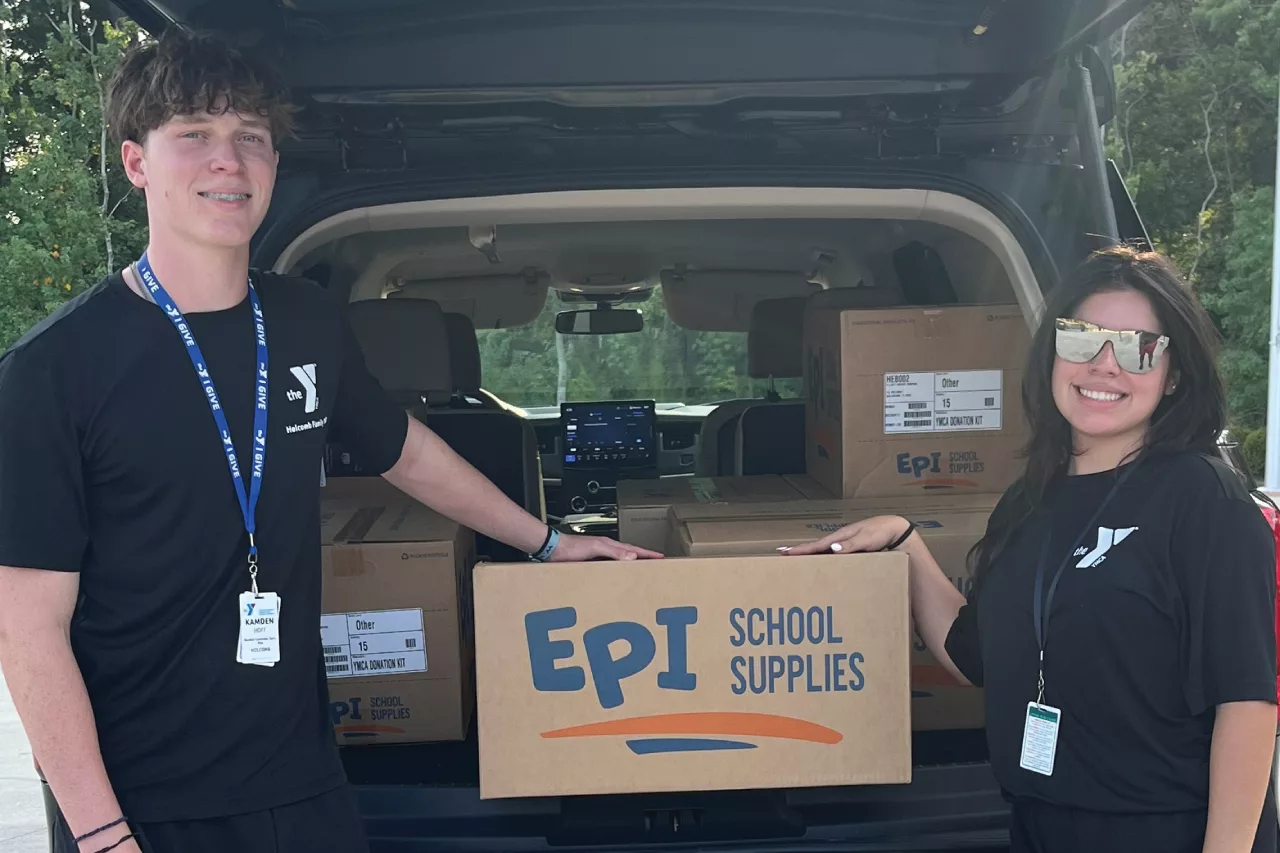 Two people standing in front of a car with boxes of school supplies.
