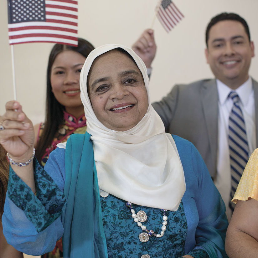 ymca-houston-give-homepage-restore-hope-and-wellbeing A group of new American citizens smiles into the camera and waves small American flags