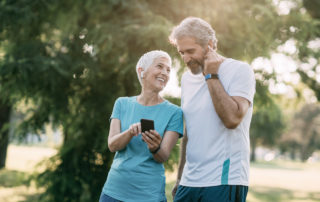 Happy senior couple using smart phone after jogging in the public park.