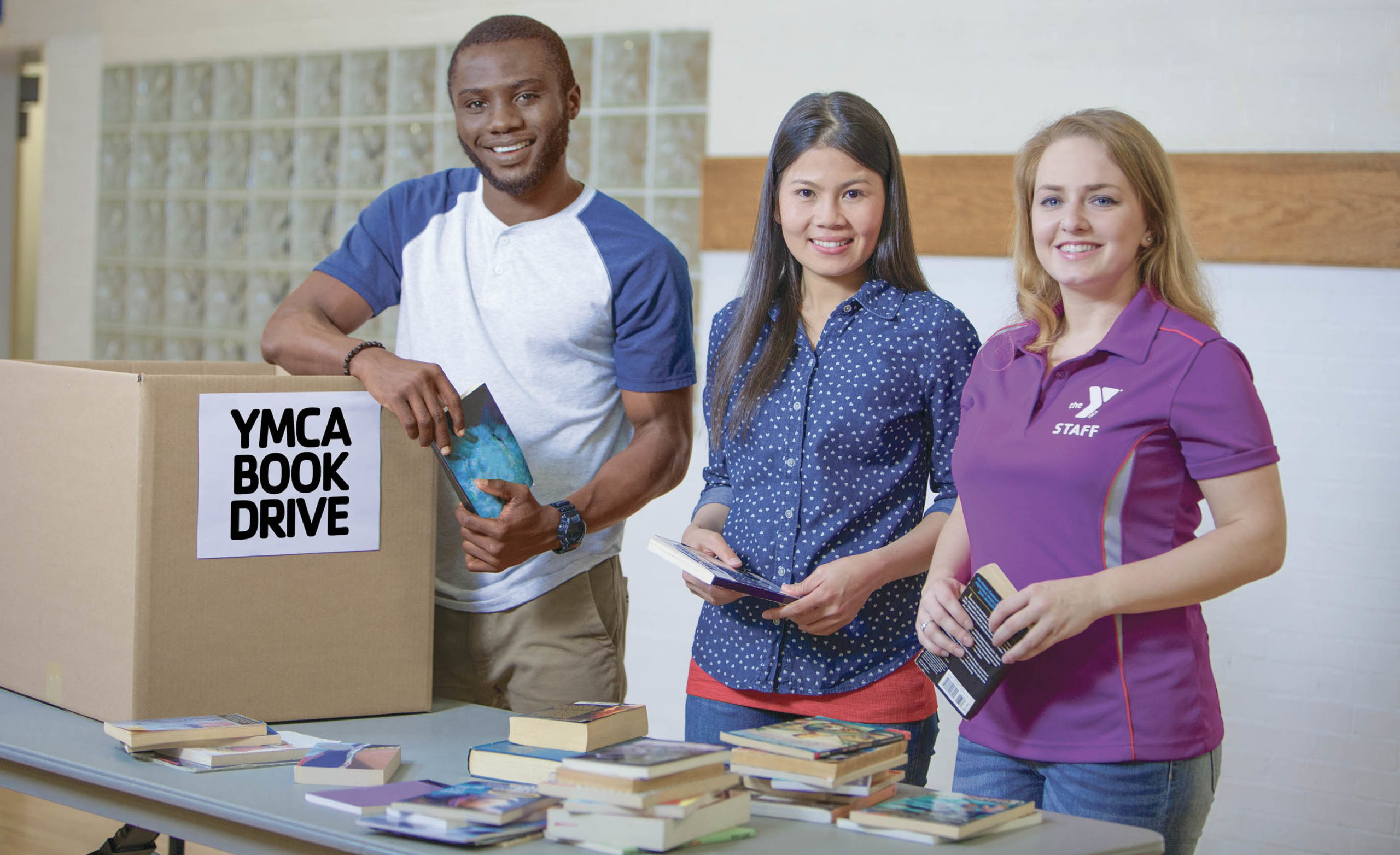 Three multiethnic volunteers stand at a book drive table