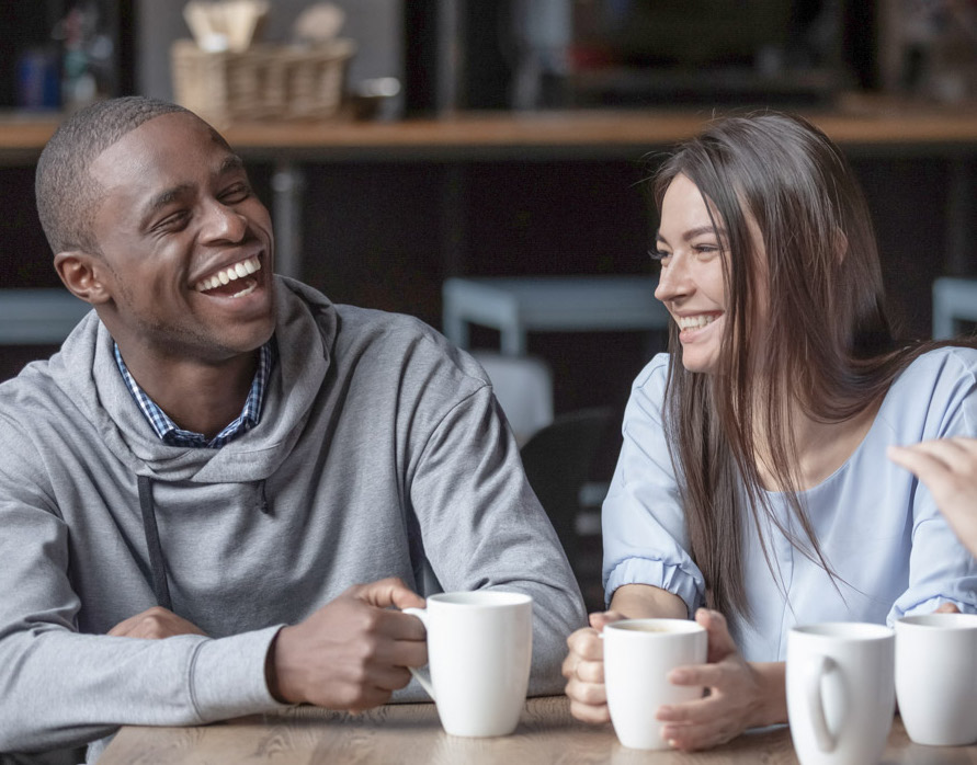 Multiracial friends girls and guys having fun laughing drinking coffee tea in coffeehouse, happy diverse young people talking joking sitting together at cafe table, multicultural friendship concept