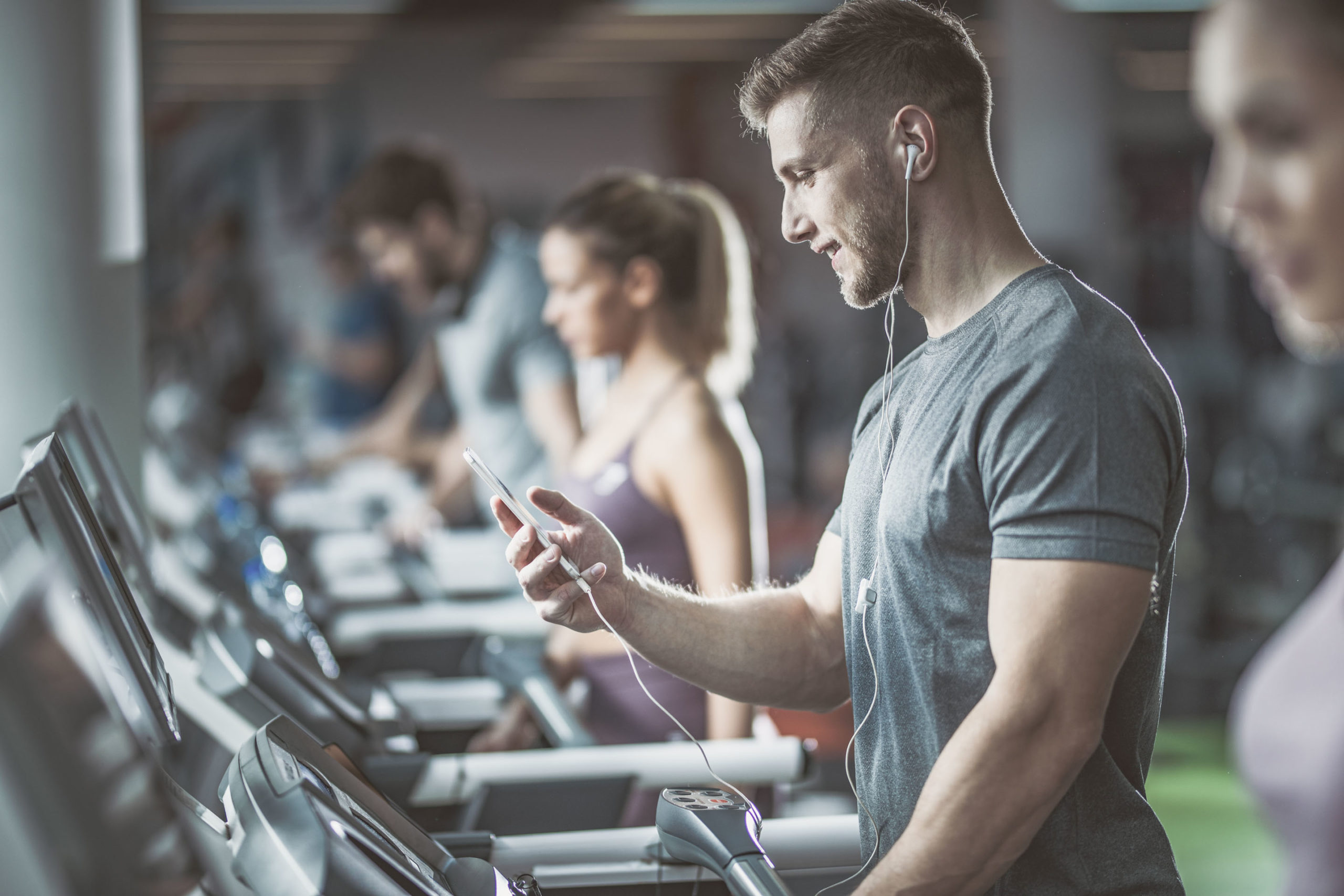 Athletic man exercising on treadmill in a gym and listening music over his cell phone.
