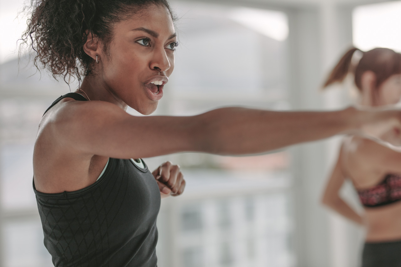 African American young woman doing intense punching work out at the gym. Young slim woman in sportswear doing exercise during intensive circuit training.