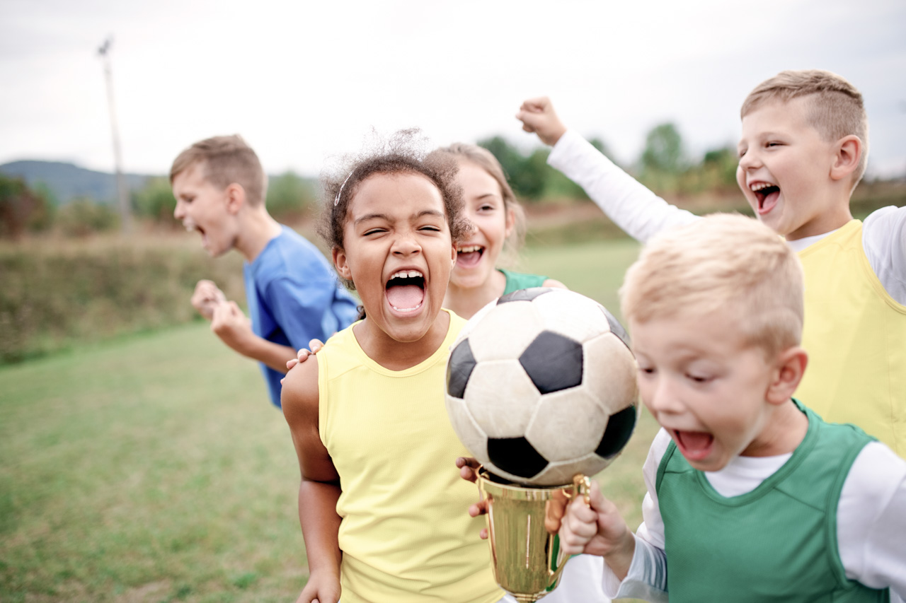 Cheerful small boys and girls, shouting on a soccer field