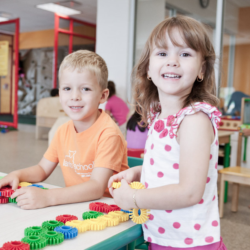 Two young children playing with toys at a table, smiling at the camera