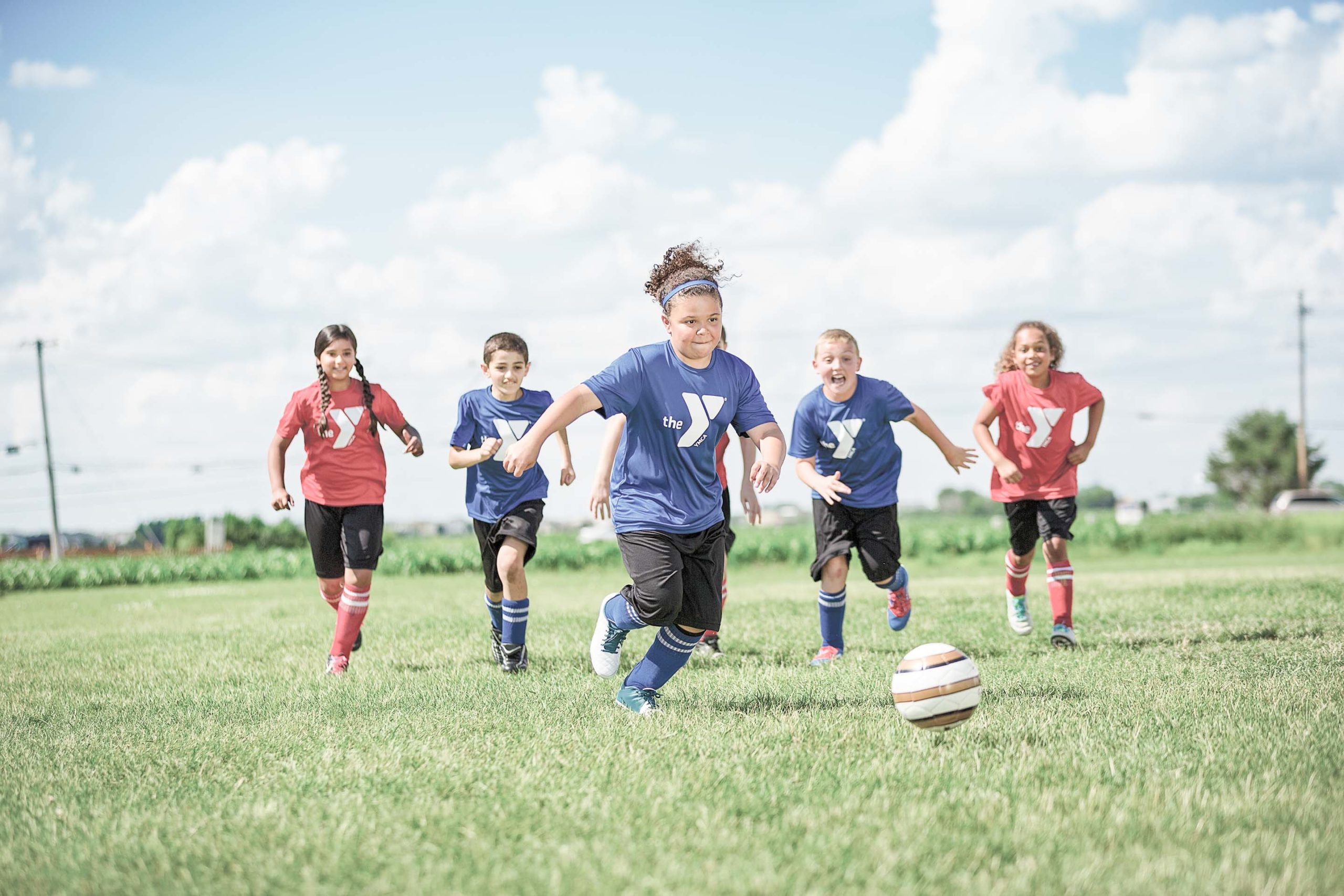 A group of middle school aged children play soccer on a field, running towards the camera