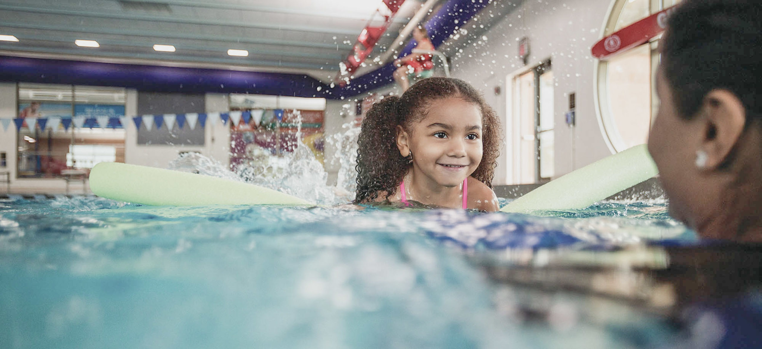 A young girl learns to swim in an indoor pool