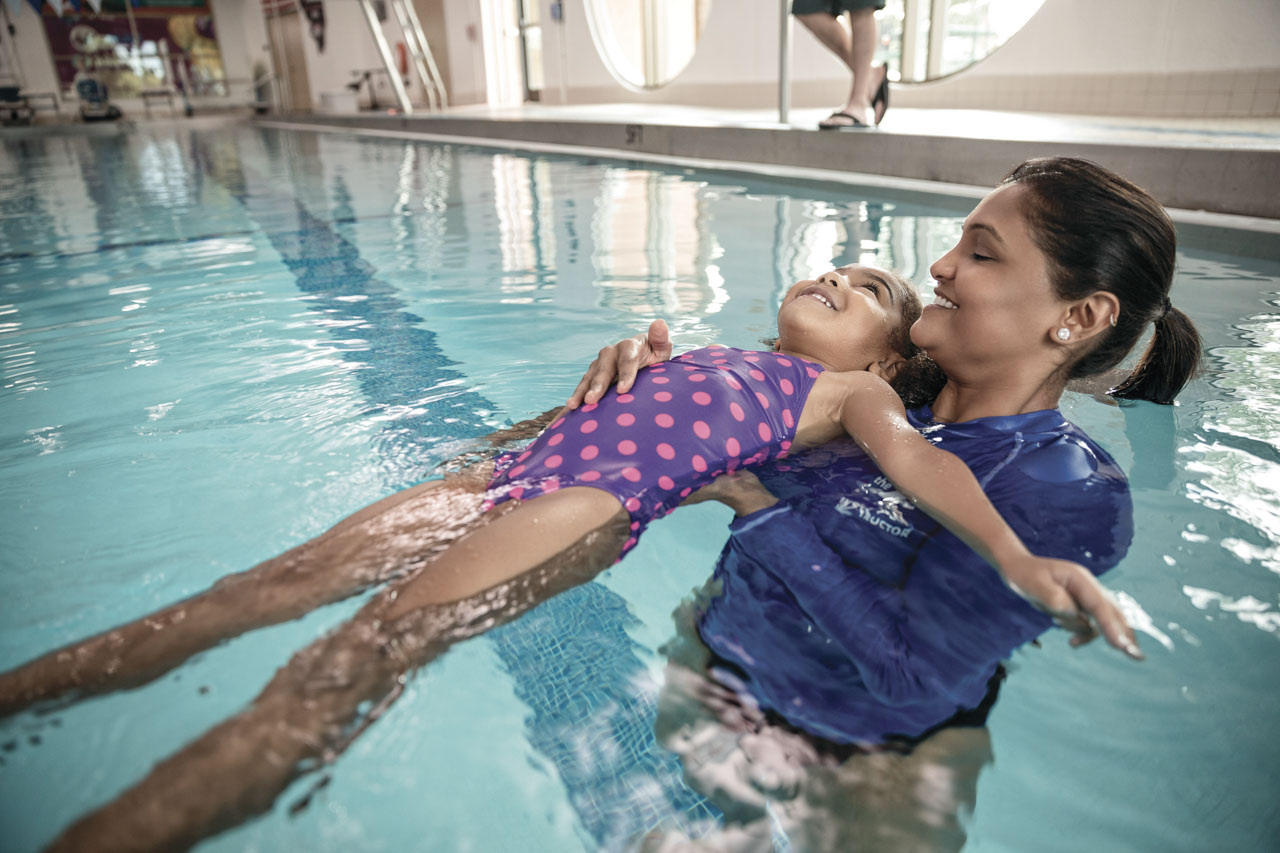 woman giving young girl swimming lessons in an indoor pool