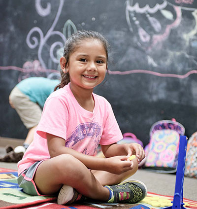 young girl sitting and drawing with chalk