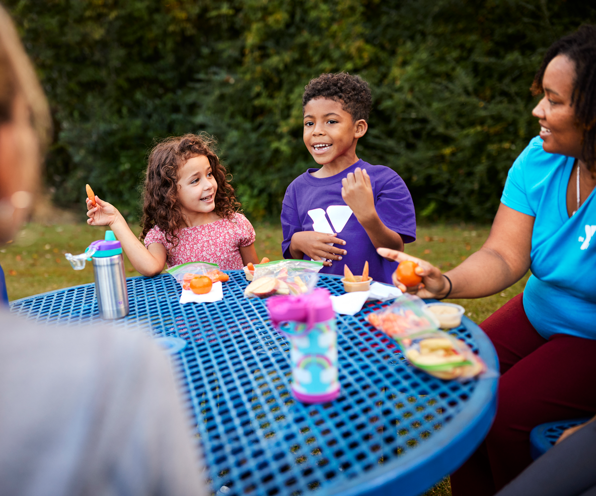 A group of young kids and adults enjoying their snack outdoors