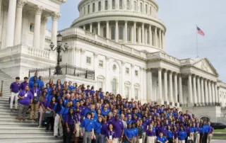 A diverse group of individuals dressed in blue posing for a photo in front of a white building