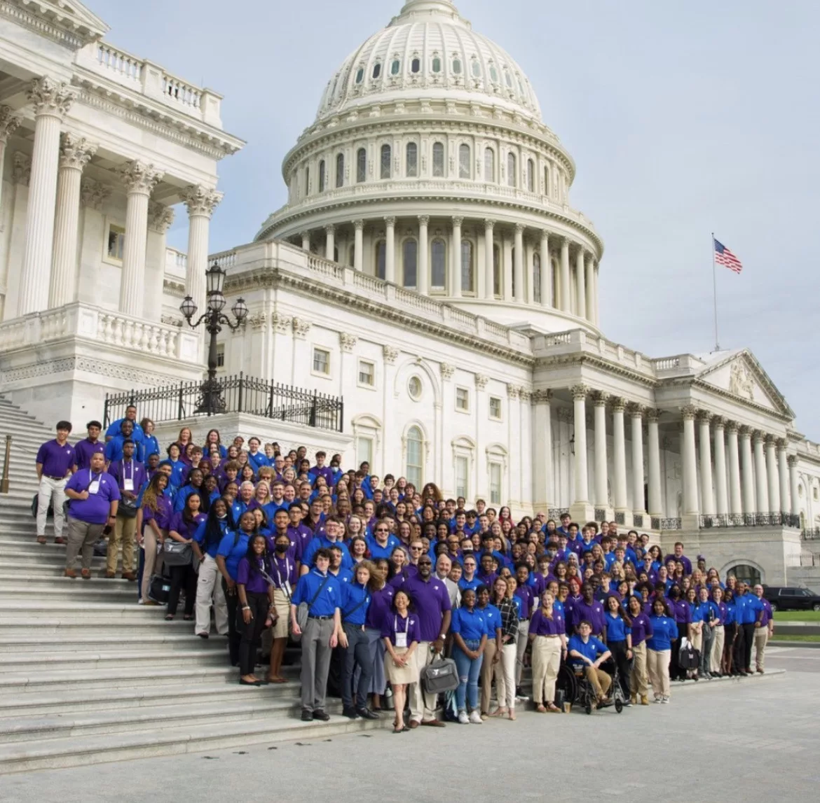 A diverse group of individuals dressed in blue posing for a photo in front of a white building